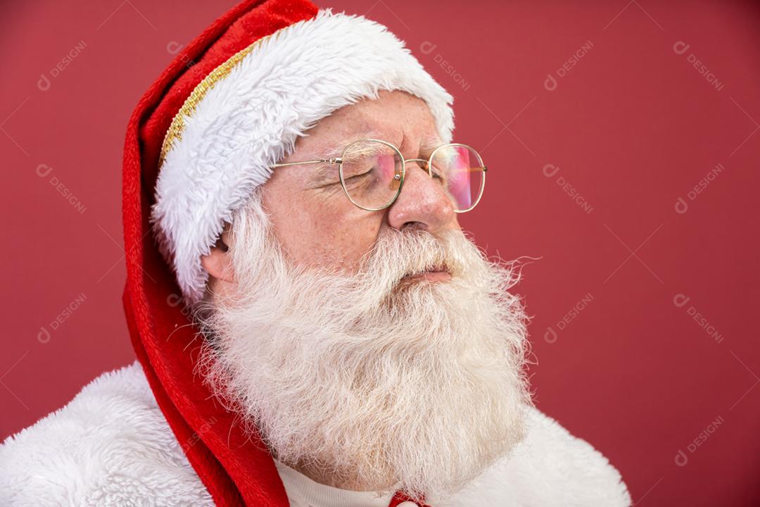 Verdadeiro Papai Noel com um fundo vermelho, usando óculos, luvas e um chapéu olhando de lado