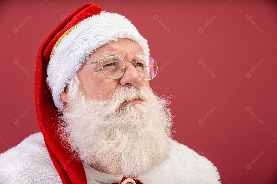 Verdadeiro Papai Noel com um fundo vermelho, usando óculos, luvas e um chapéu olhando de lado