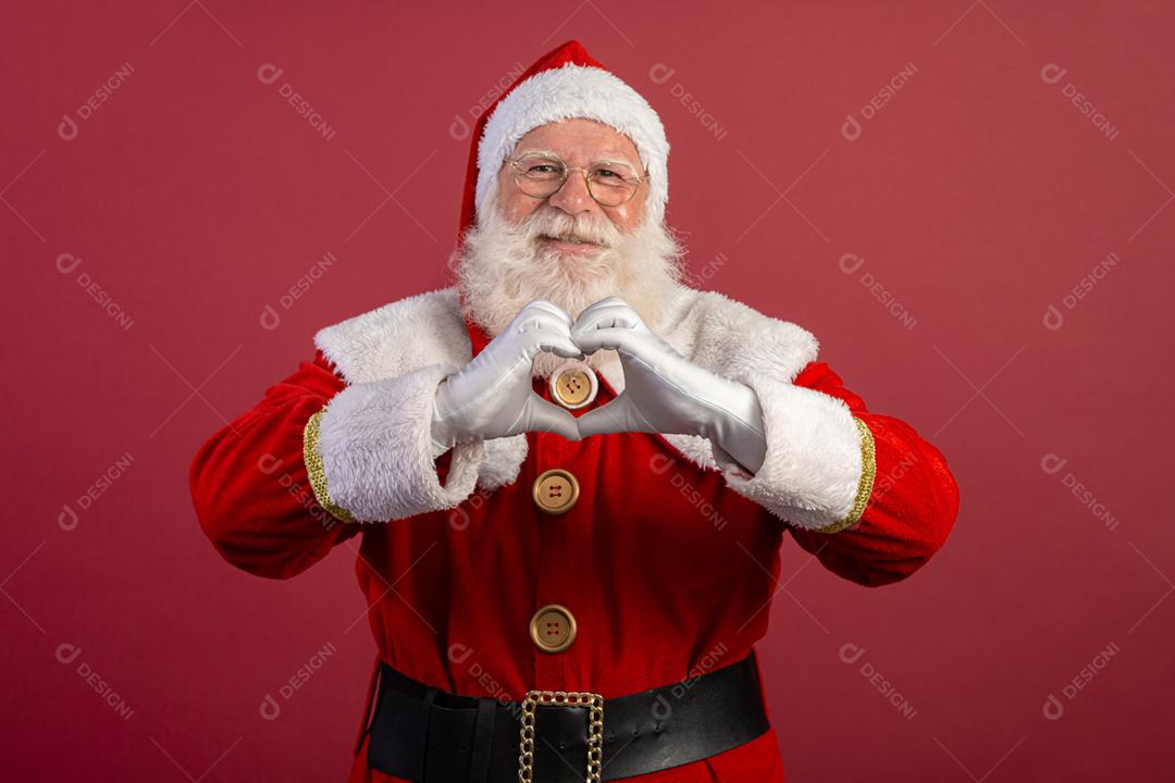 Papai Noel fazendo sinal de coração com as mãos e fundo vermelho.