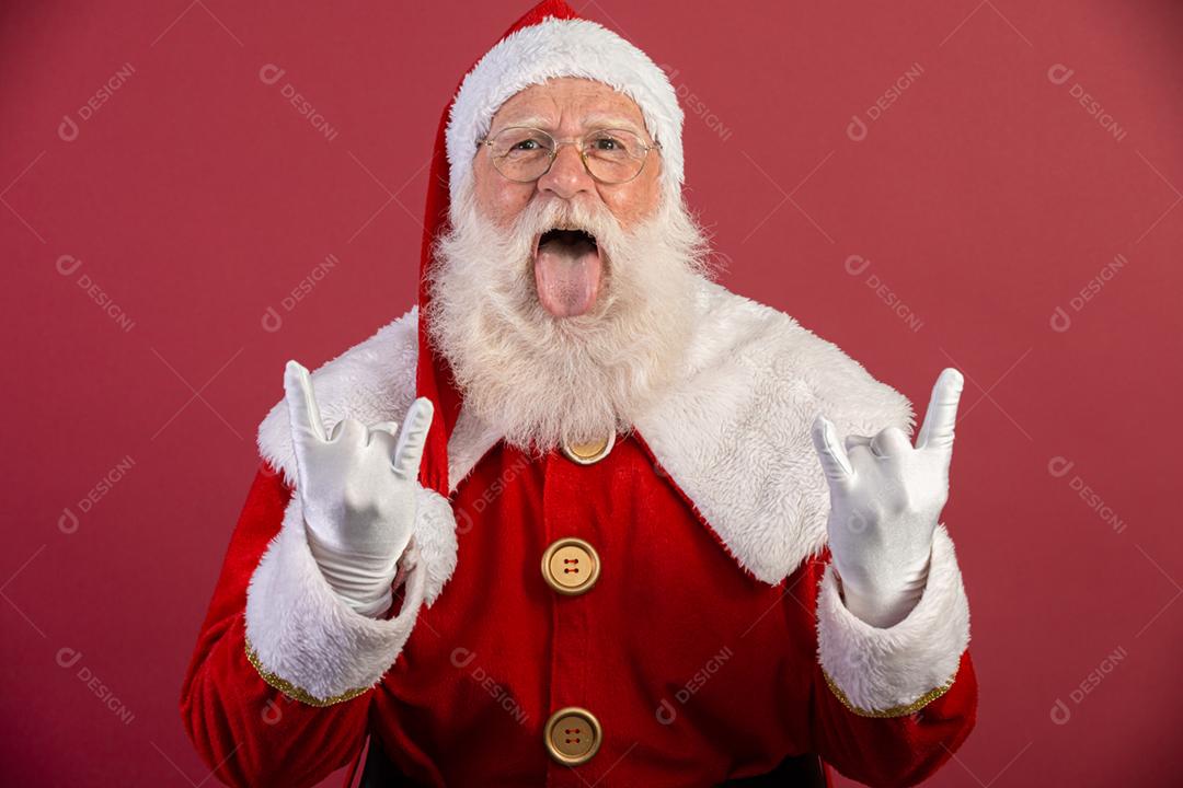 Papai Noel fazendo sinal de rock n roll com as mãos e fundo vermelho.