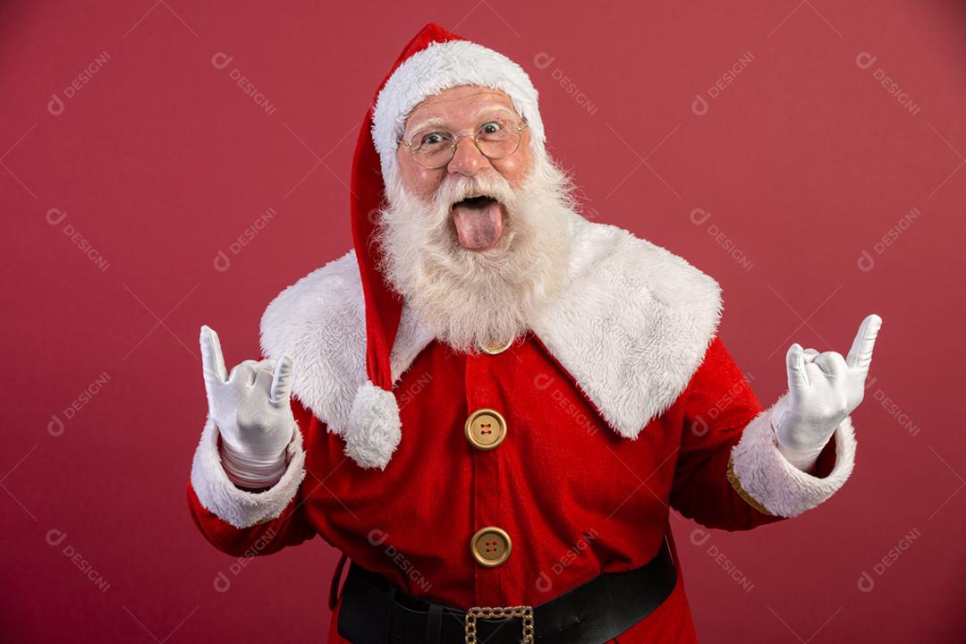 Papai Noel fazendo sinal de rock n roll com as mãos e fundo vermelho.