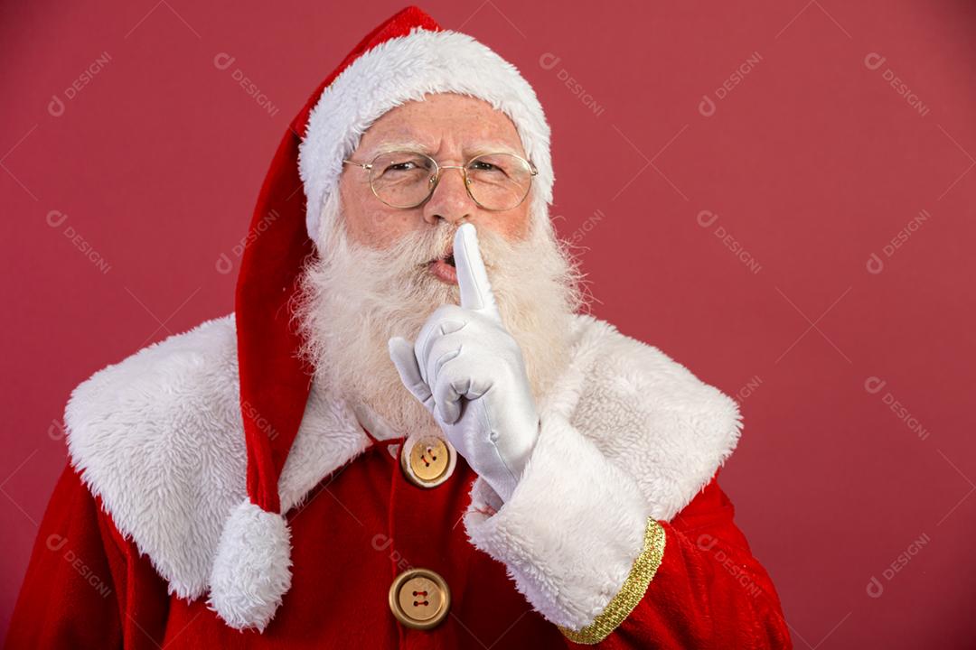 Papai Noel mantendo o dedo indicador pela boca e olhando para a câmera. Shh! Guarde segredo. Silencioso confidencial