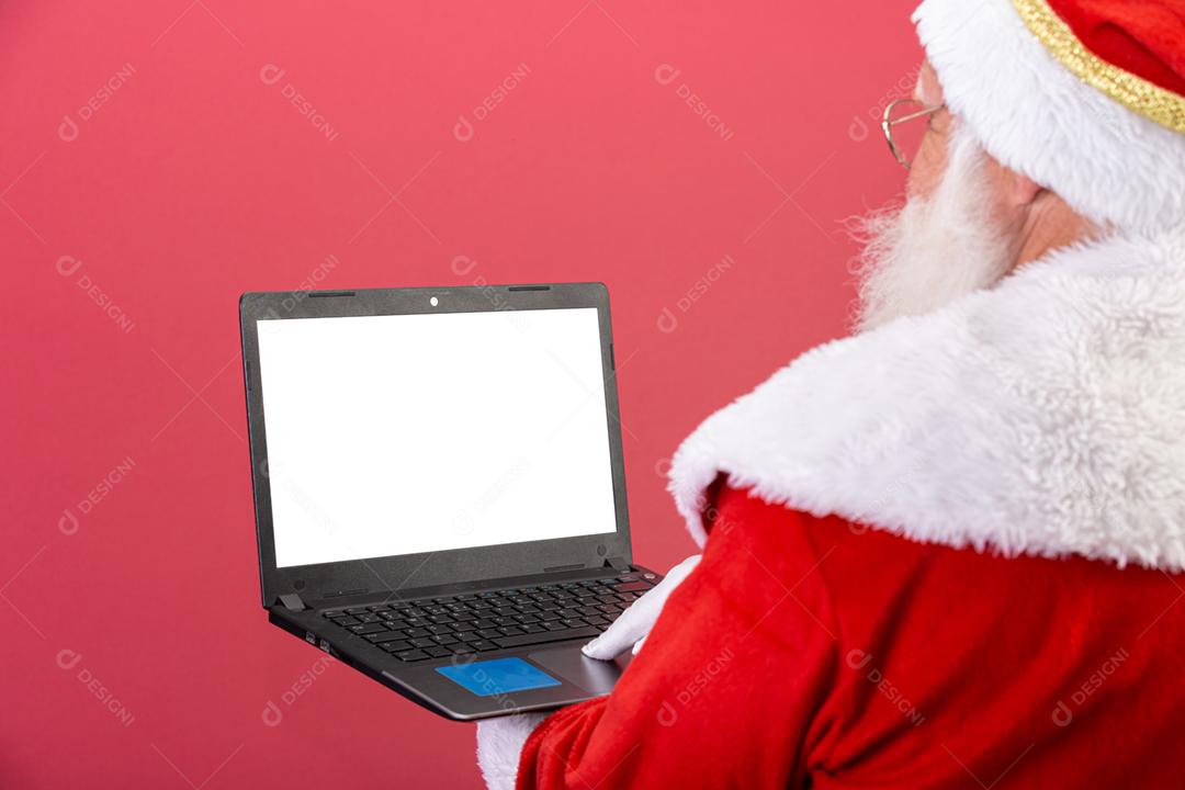 Papai Noel usando um laptop em fundo vermelho.