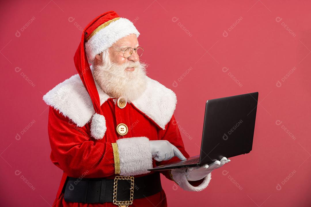 Papai Noel usando um laptop em fundo vermelho.