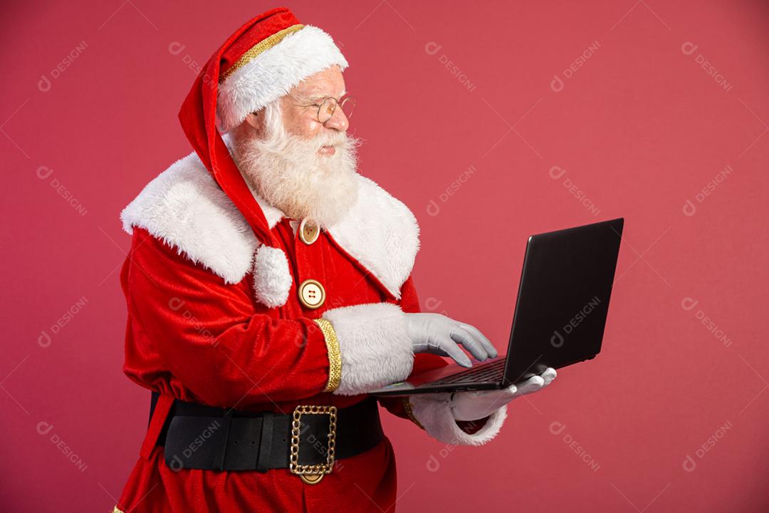 Papai Noel usando um laptop em fundo vermelho.