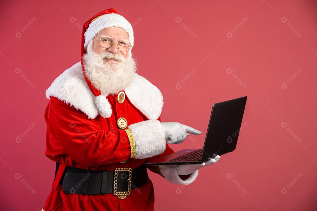 Papai Noel usando um laptop em fundo vermelho.