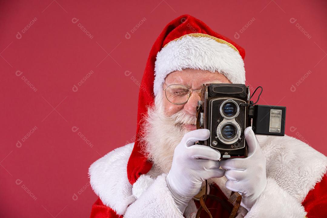 Papai Noel segurando a câmera vintage. Retrato isolado em fundo vermelho.