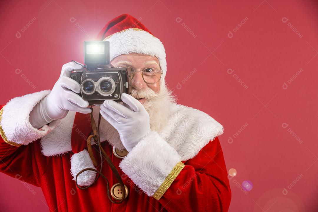 Papai Noel segurando a câmera vintage. Retrato isolado em fundo vermelho.