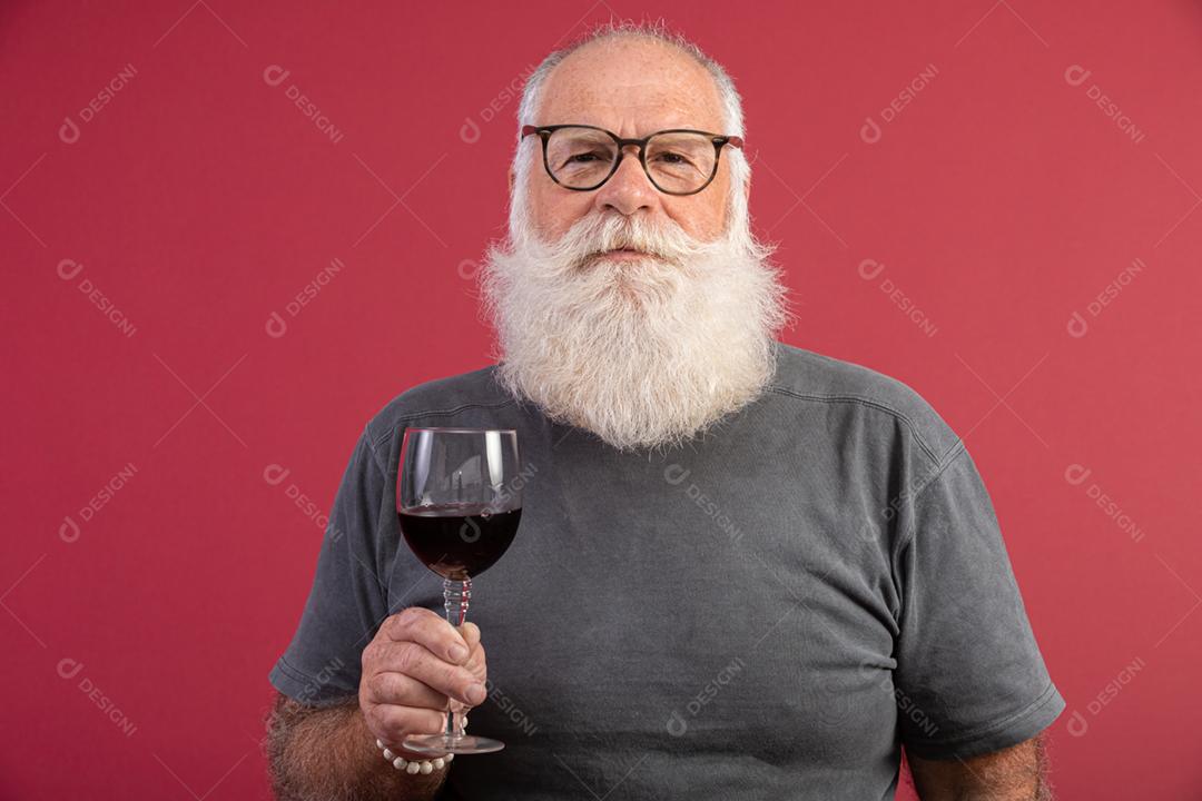 Homem barbudo elegante e bonito bebendo vinho tinto sobre fundo vermelho. Sommelier de homem