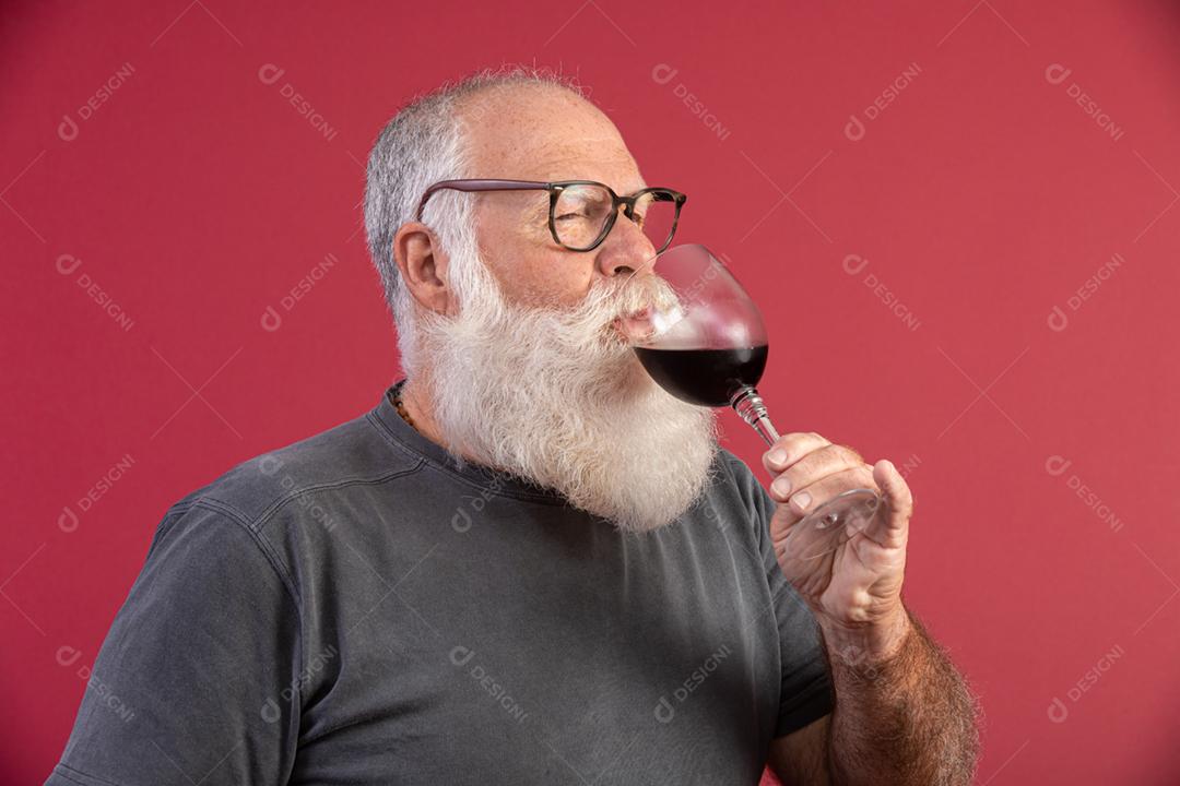 Homem barbudo elegante e bonito bebendo vinho tinto sobre fundo vermelho. Sommelier de homem
