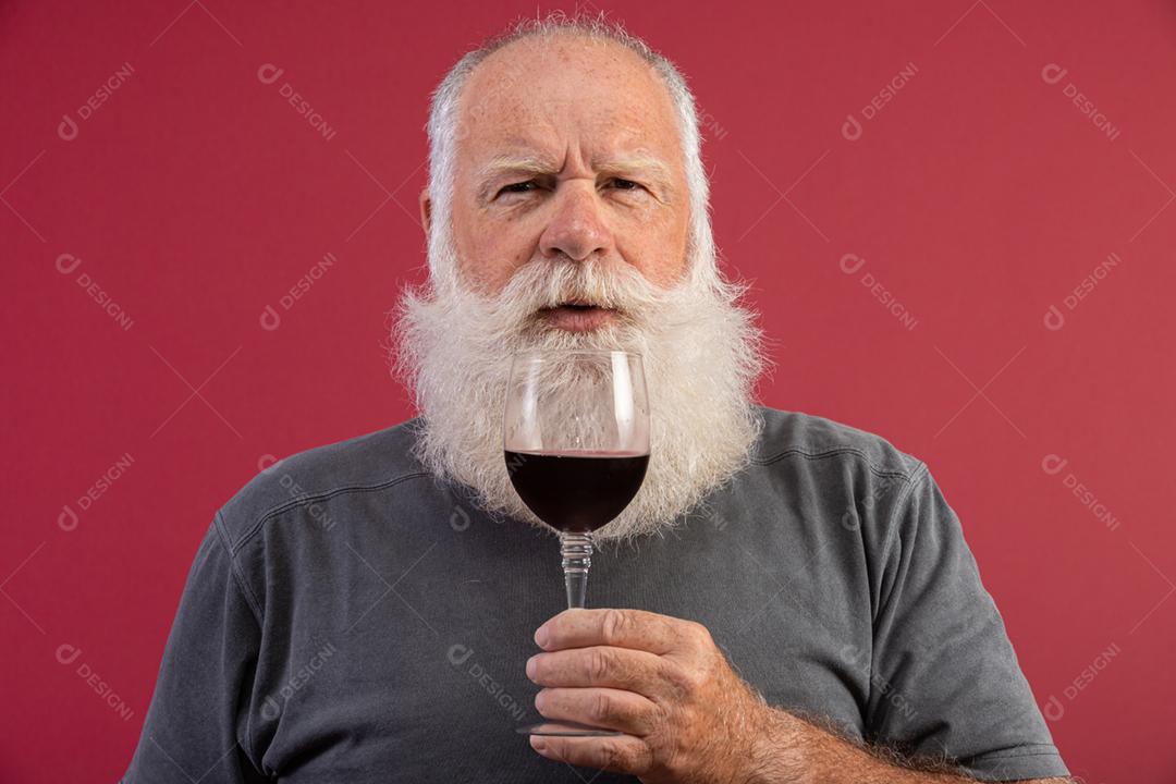 Homem barbudo elegante e bonito bebendo vinho tinto sobre fundo vermelho. Sommelier de homem