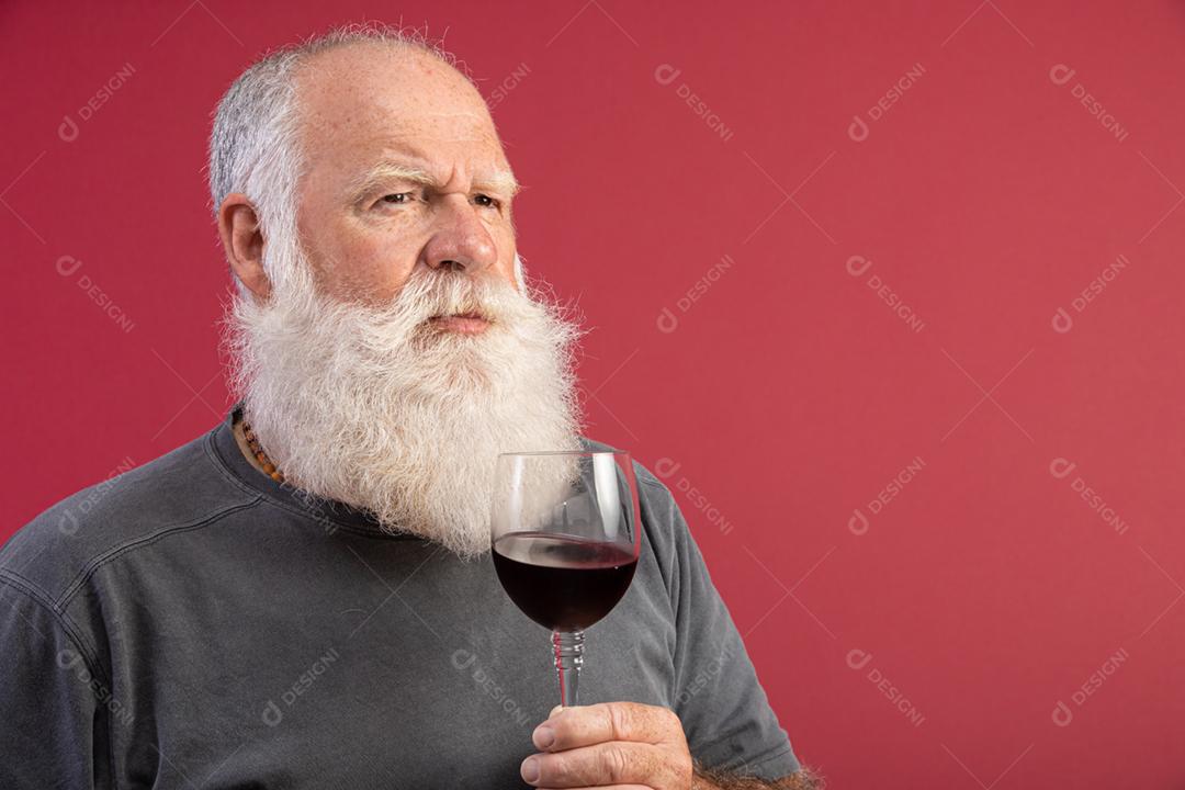Homem barbudo elegante e bonito bebendo vinho tinto sobre fundo vermelho. Sommelier de homem