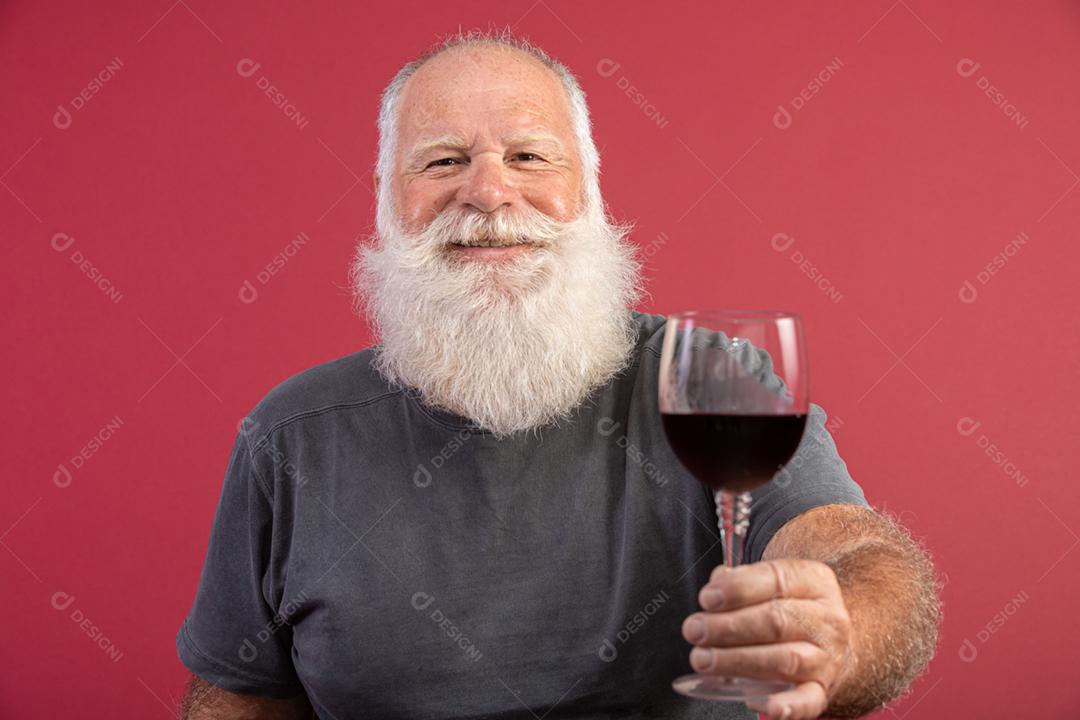 Homem barbudo elegante e bonito bebendo vinho tinto sobre fundo vermelho. Sommelier de homem