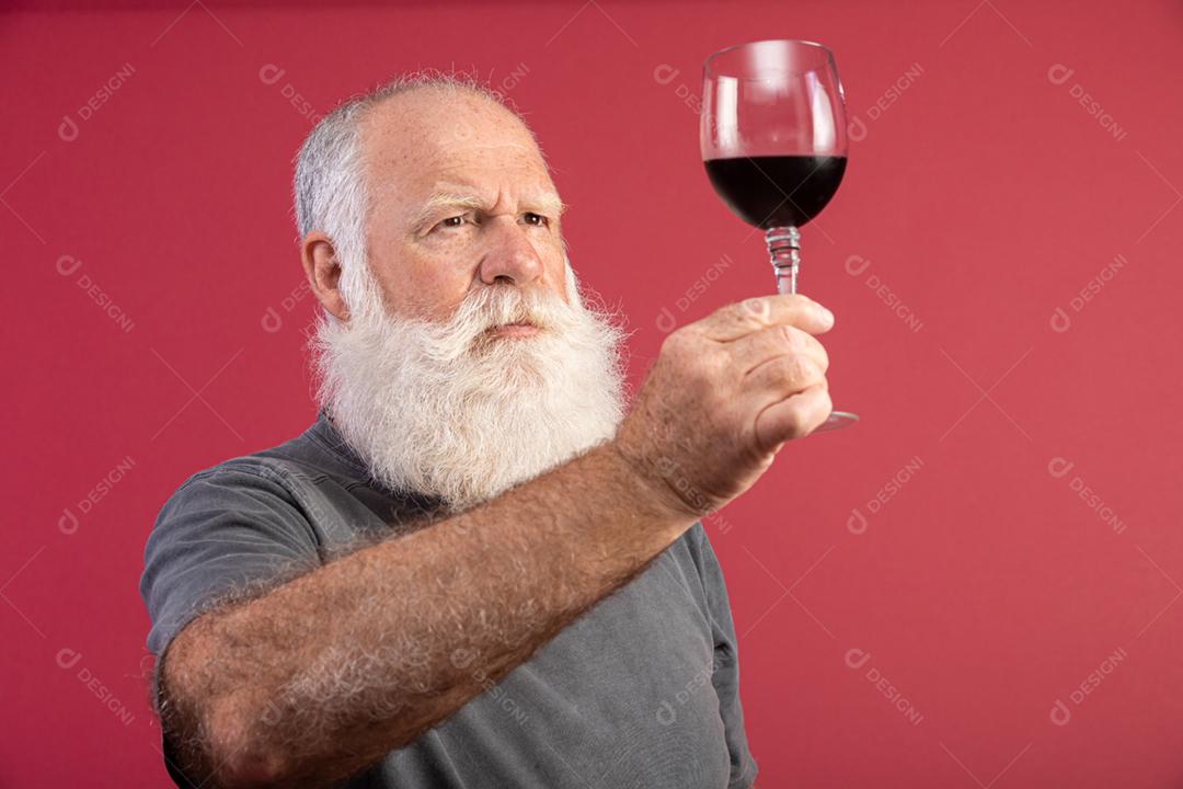Homem barbudo elegante e bonito bebendo vinho tinto sobre fundo vermelho. Sommelier de homem