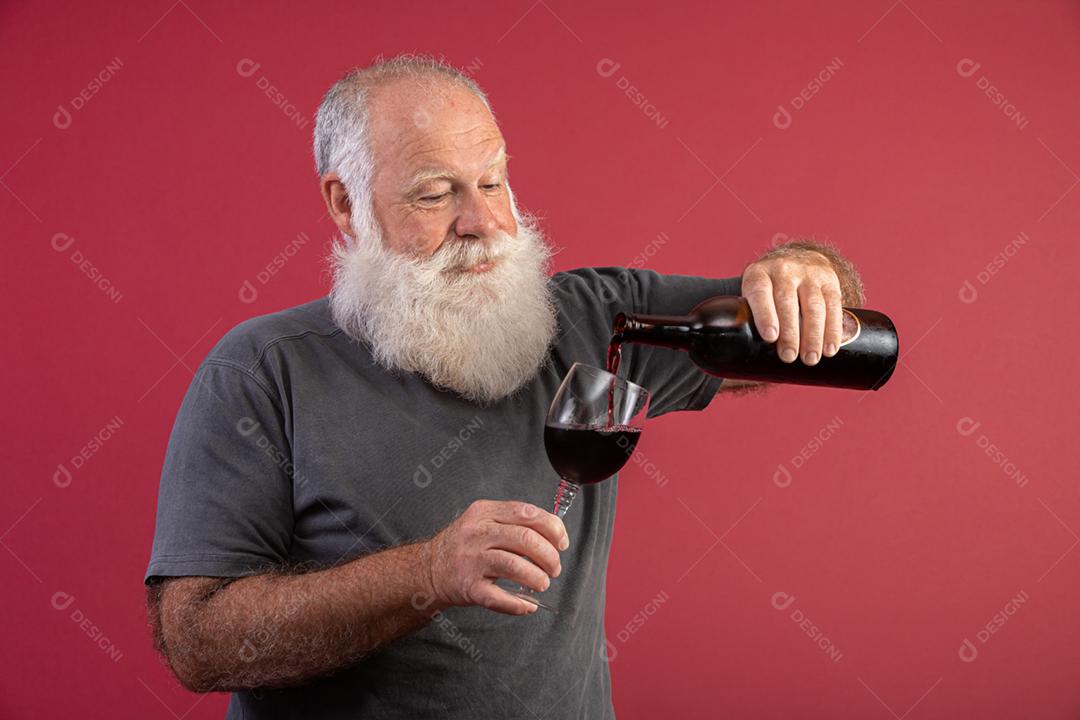 Homem barbudo elegante e bonito bebendo vinho tinto sobre fundo vermelho. Sommelier de homem