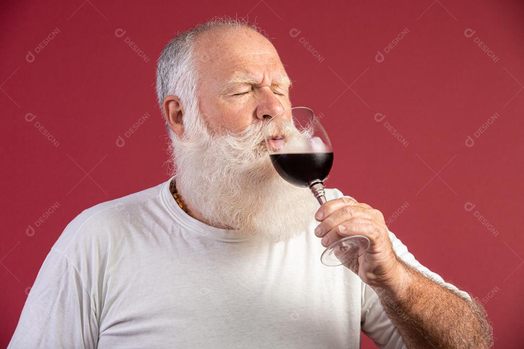 Homem barbudo elegante e bonito bebendo vinho tinto sobre fundo vermelho. Sommelier de homem