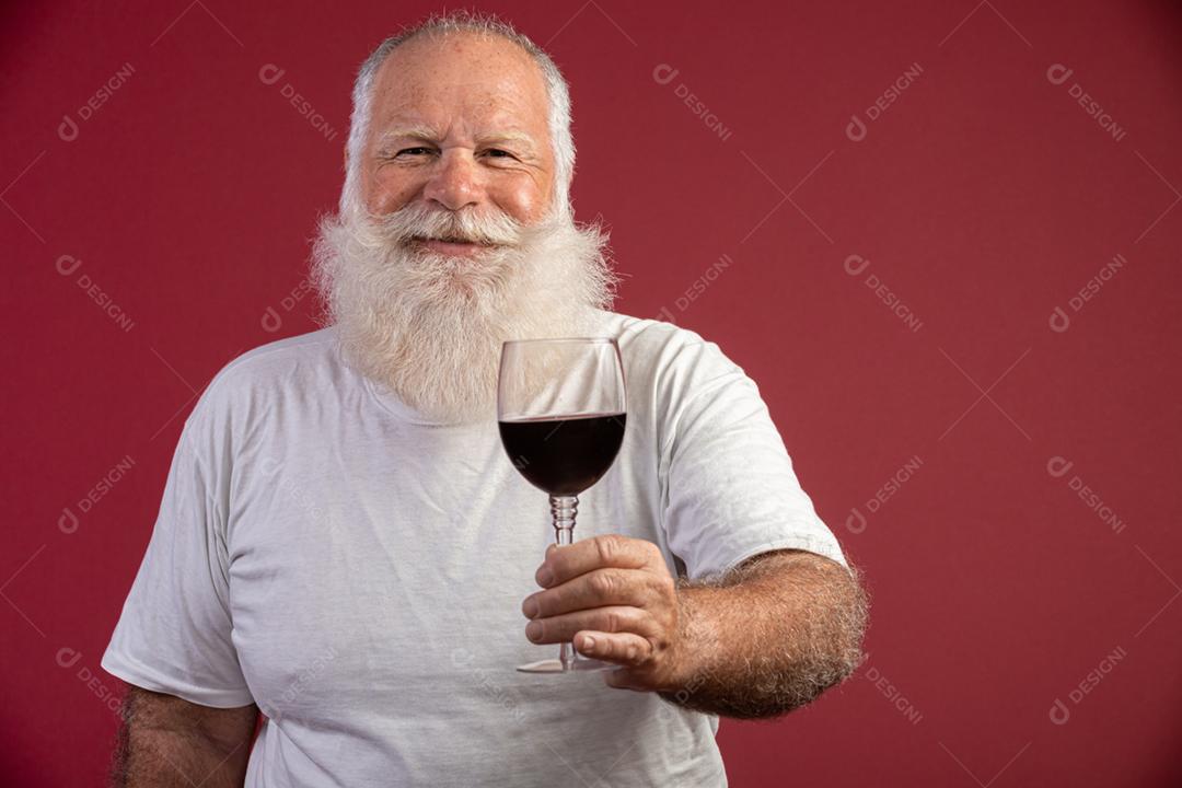 Homem barbudo elegante e bonito bebendo vinho tinto sobre fundo vermelho. Sommelier de homem