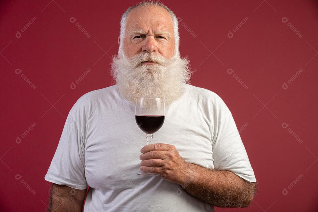 Homem barbudo elegante e bonito bebendo vinho tinto sobre fundo vermelho. Sommelier de homem