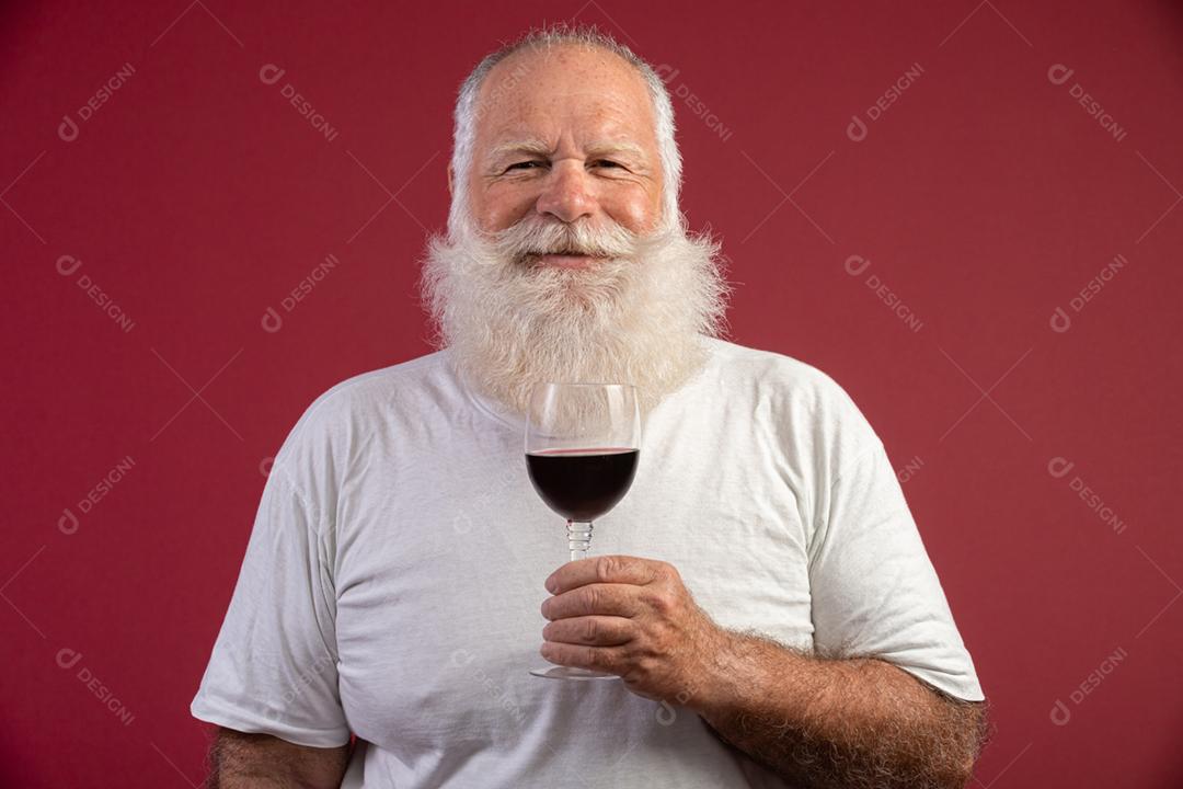 Homem barbudo elegante e bonito bebendo vinho tinto sobre fundo vermelho. Sommelier de homem