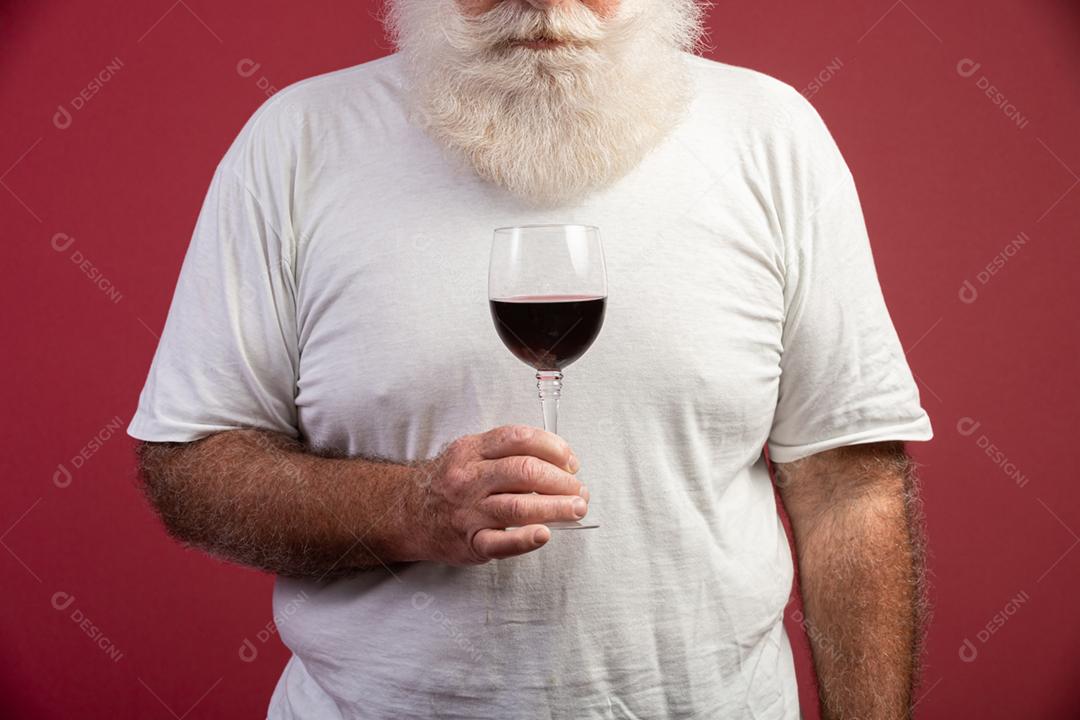 Homem barbudo elegante e bonito bebendo vinho tinto sobre fundo vermelho. Sommelier de homem