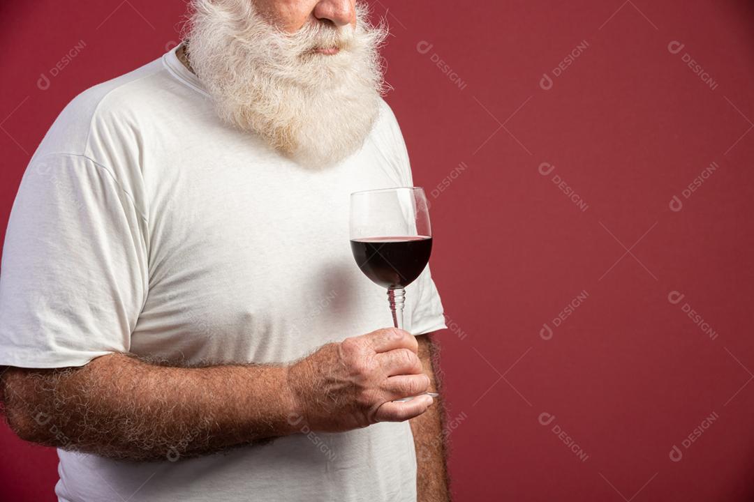 Homem barbudo elegante e bonito bebendo vinho tinto sobre fundo vermelho. Sommelier de homem