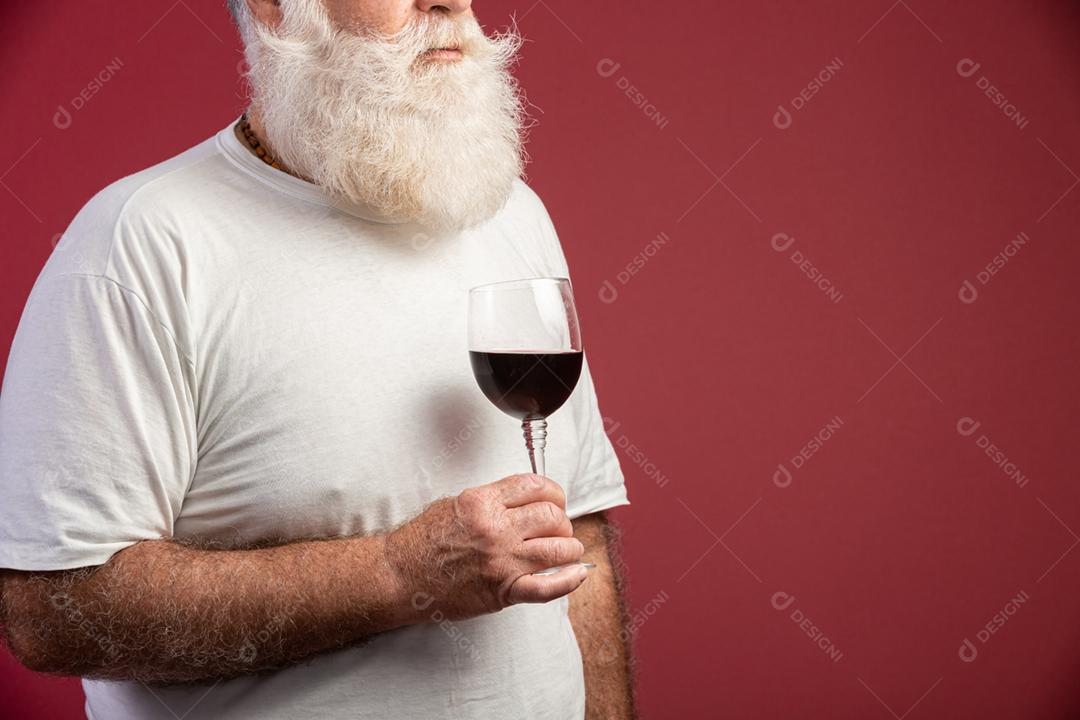 Homem barbudo elegante e bonito bebendo vinho tinto sobre fundo vermelho. Sommelier de homem