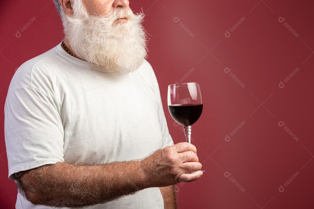 Homem barbudo elegante e bonito bebendo vinho tinto sobre fundo vermelho. Sommelier de homem