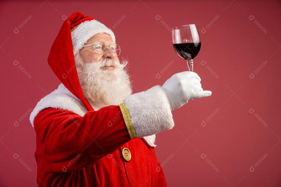 Noel segurando um copo de vinho na mão. Papai Noel sobre um fundo vermelho. Bebida tradicional de fim de ano. Promoção de Natal de vinho.