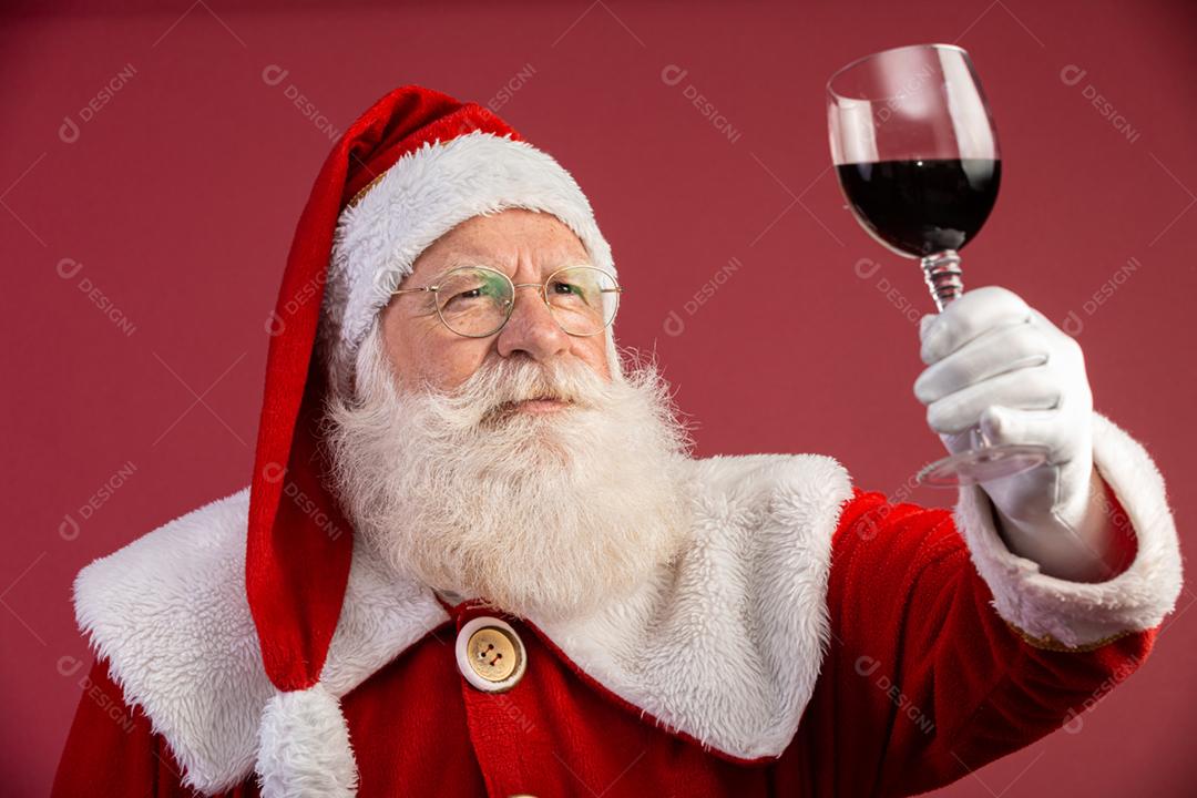 Noel segurando um copo de vinho na mão. Papai Noel sobre um fundo vermelho. Bebida tradicional de fim de ano. Promoção de Natal de vinho.