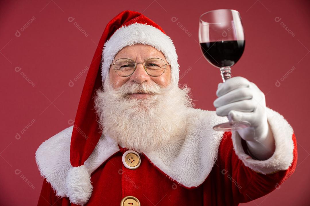 Noel segurando um copo de vinho na mão. Papai Noel sobre um fundo vermelho. Bebida tradicional de fim de ano. Promoção de Natal de vinho.
