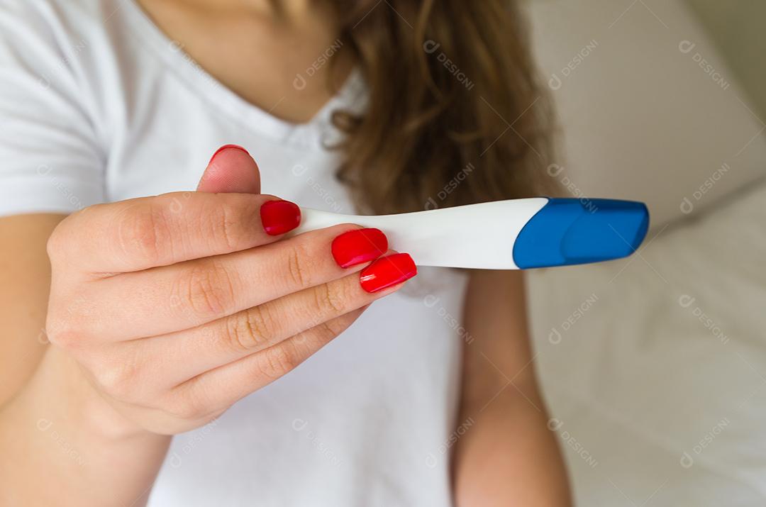 Mulher segurando teste de gravidez sobre fundo branco. Foco seletivo