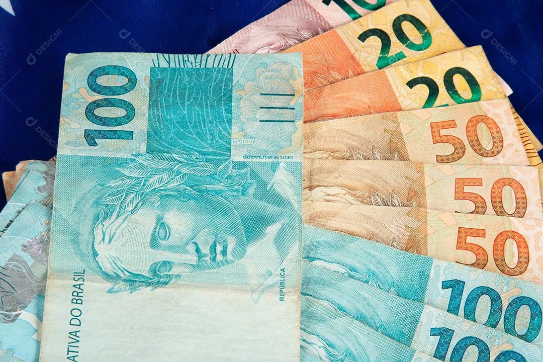 Notas de dinheiro brasileiras com bandeira do Brasil em segundo plano