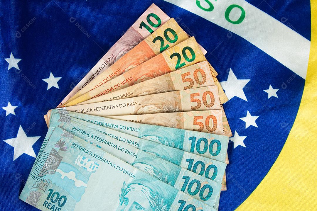 Notas de dinheiro brasileiras com bandeira do Brasil em segundo plano