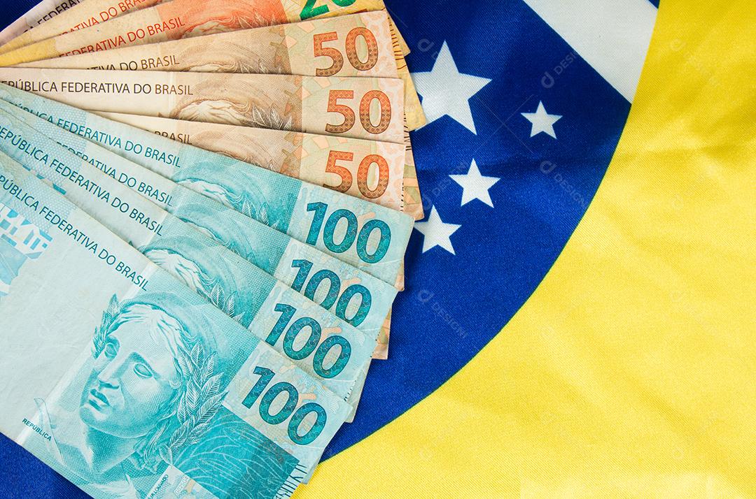 Notas de dinheiro brasileiras com bandeira do Brasil em segundo plano