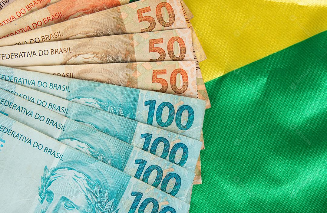 Notas de dinheiro brasileiras com bandeira do Brasil em segundo plano