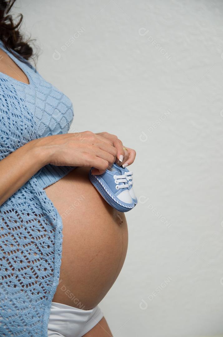 Grande conceito de gravidez, sapatos pequenos para o feto na barriga da mulher grávida.