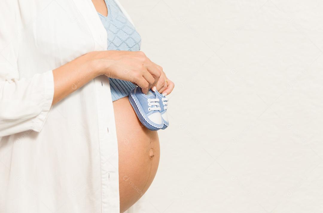 Grande conceito de gravidez, sapatos pequenos para o feto na barriga da mulher grávida.
