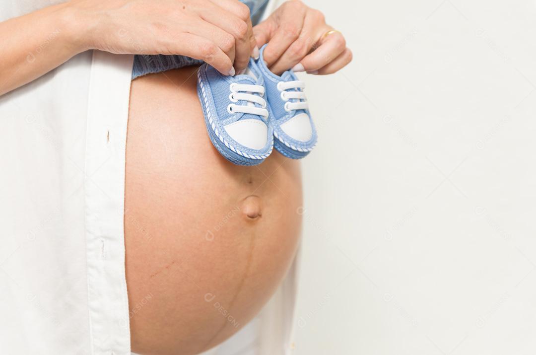 Grande conceito de gravidez, sapatos pequenos para o feto na barriga da mulher grávida.