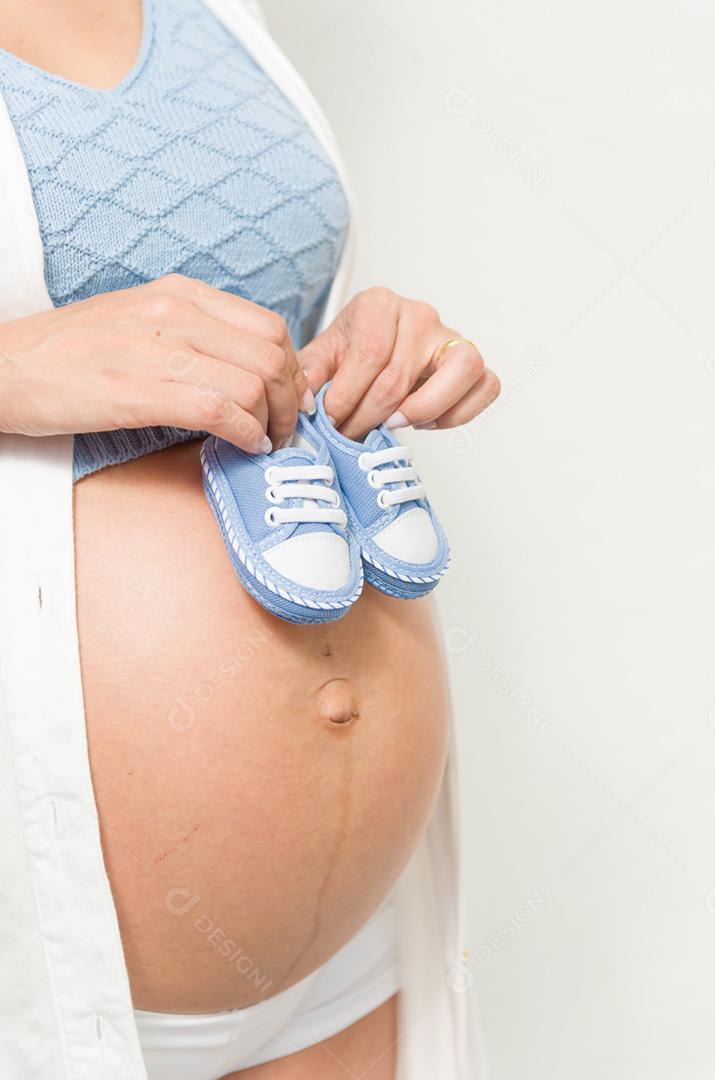 Grande conceito de gravidez, sapatos pequenos para o feto na barriga da mulher grávida.