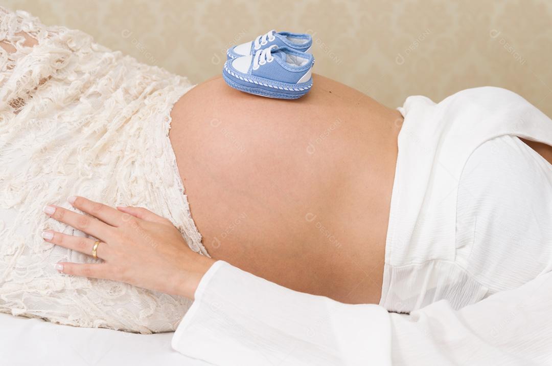 Grande conceito de gravidez, sapatos pequenos para o feto na barriga da mulher grávida.