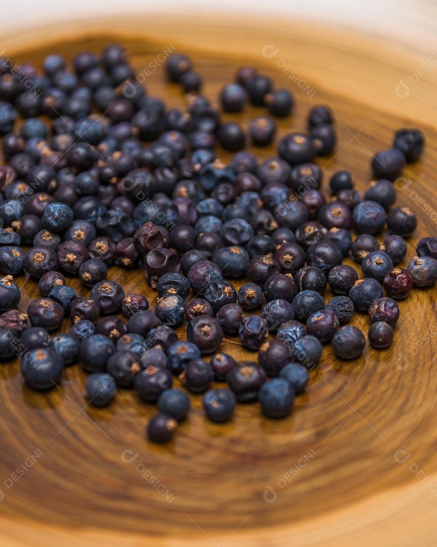 Uma pilha de bagas de zimbro fecha-se sobre fundo de madeira sem foco.