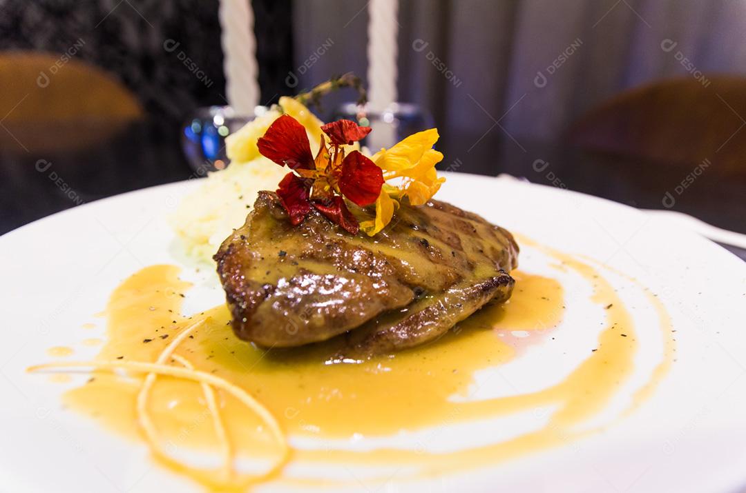 Peito de pato com molho de laranja no prato decorado com flores.