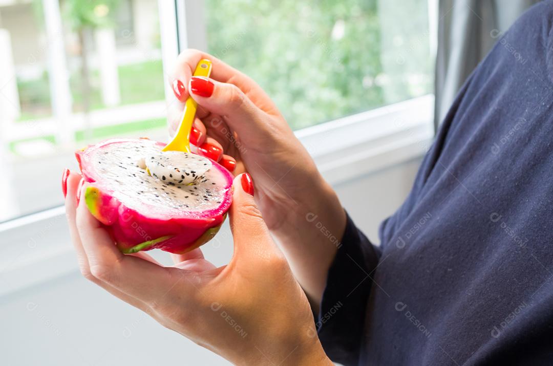 Mão de mulher comendo pitaya com colher colorida.