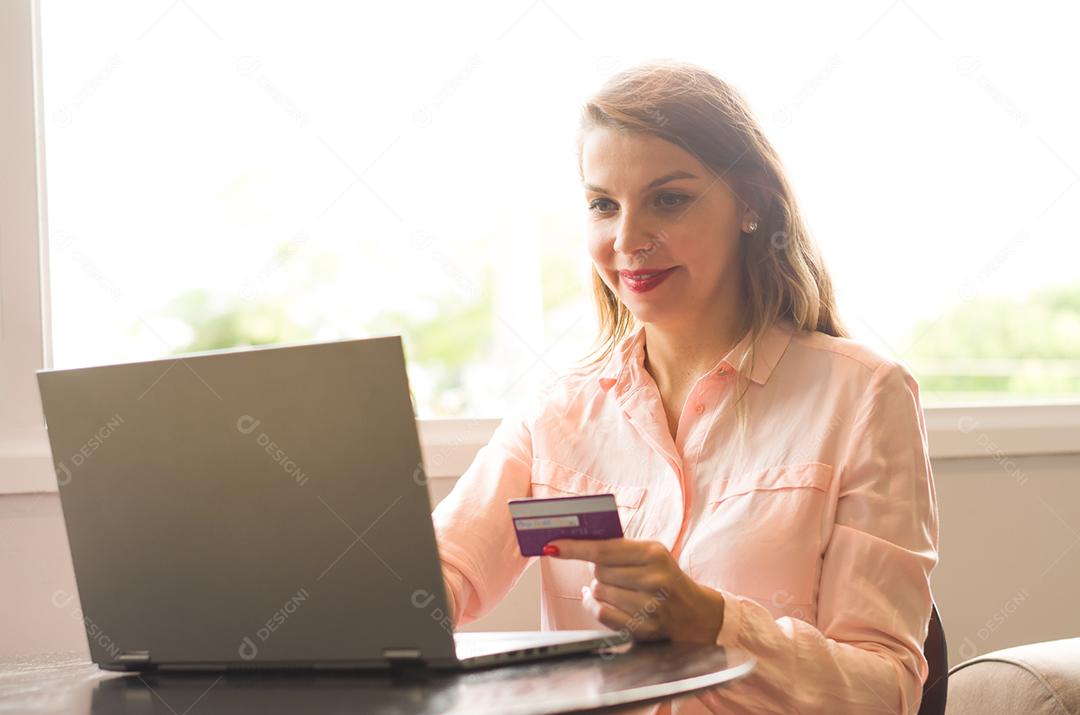 Jovem loira caucasiana feliz comprando na internet, cartão de crédito na mão.
