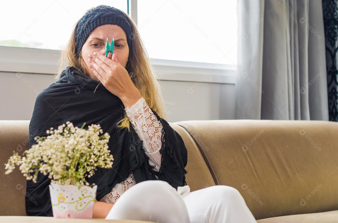 Grande conceito de alergia, rinite ao pólen. Jovem mulher loira com pega no nariz para plantar, flor.