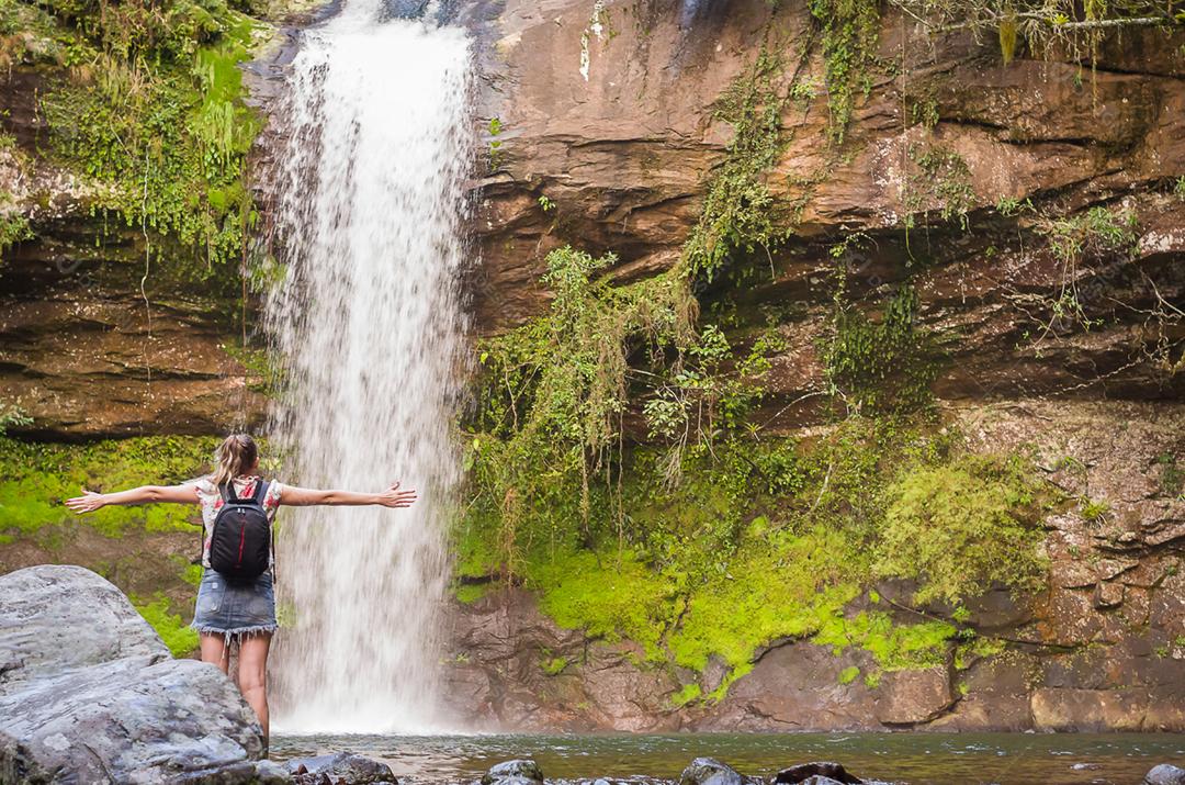 Uma cachoeira para relaxar, mulher de braços abertos para a cachoeira.