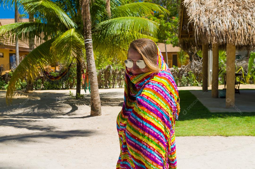 Jovem turista loira coberta por sarongue típico baiano para se proteger do sol forte do Brasil.