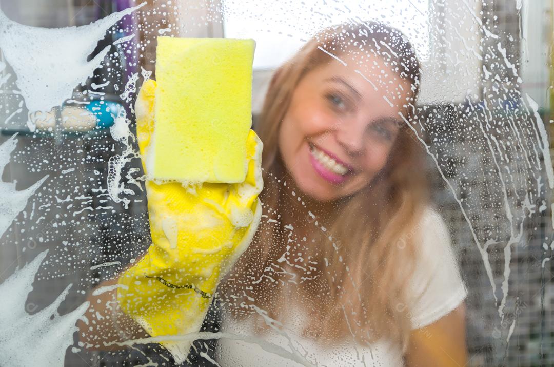 Grande conceito de limpeza doméstica, jovem loira limpando vidro do banheiro.
