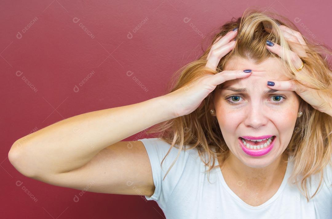 Conceito de preocupação, mulher com as duas mãos na cabeça sobre fundo vermelho.