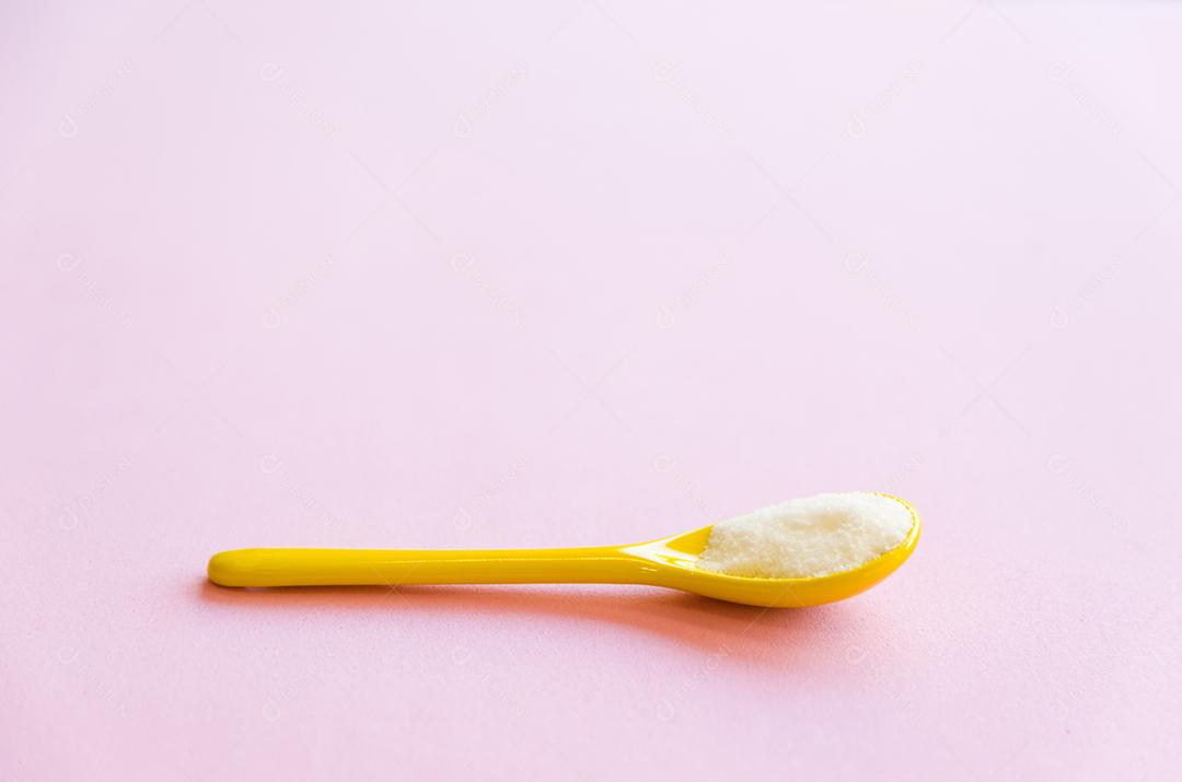 Colher com açúcar close-up em um fundo rosa